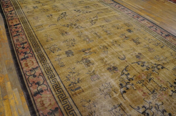 Faded gold rug featuring scattered dark traditional designs and a pink patterned border on wood floor.