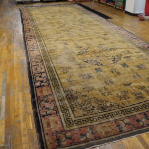 Extra-long gold rug with dark motifs, a red border, and geometric trim rests on hardwood planks.