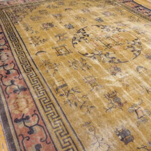 Distressed yellow rug with scattered black motifs and a detailed red and black geometric border on wood flooring.