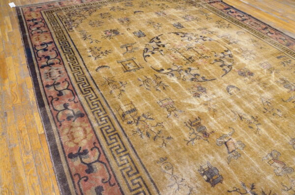 Distressed yellow rug with scattered black motifs and a detailed red and black geometric border on wood flooring.
