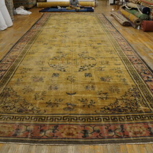 Long golden yellow rug with dark motifs and wide rose and black geometric borders on wood flooring.