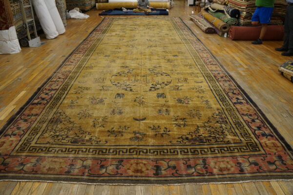 Long golden yellow rug with dark motifs and wide rose and black geometric borders on wood flooring.