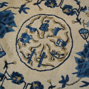 Detailed view of a cream rug featuring a central blue and tan stylized floral medallion and floral motifs.