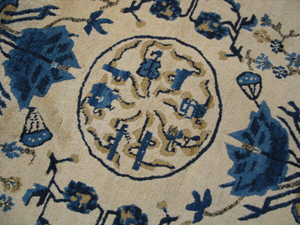 Detailed view of a cream rug featuring a central blue and tan stylized floral medallion and floral motifs.