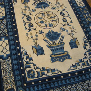 Blue and cream patterned rug featuring vase motifs and detailed borders resting on wood plank flooring.