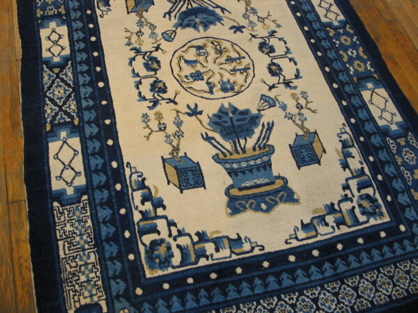 Blue and cream patterned rug featuring vase motifs and detailed borders resting on wood plank flooring.
