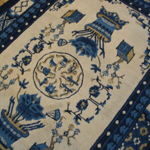 Blue and tan stylized vase pattern on a cream rug, framed by patterned borders on a wooden floor.