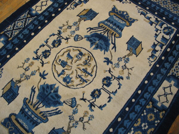 Blue and tan stylized vase pattern on a cream rug, framed by patterned borders on a wooden floor.