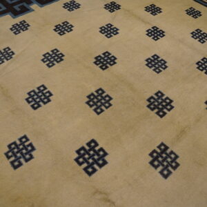 Low pile beige rug featuring dark blue repeating knots and a geometric border with light blue detail.