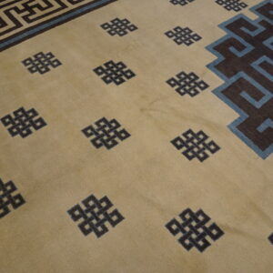 Tan rug with scattered dark knots, blue accents, and a wide geometric dark brown meander border.