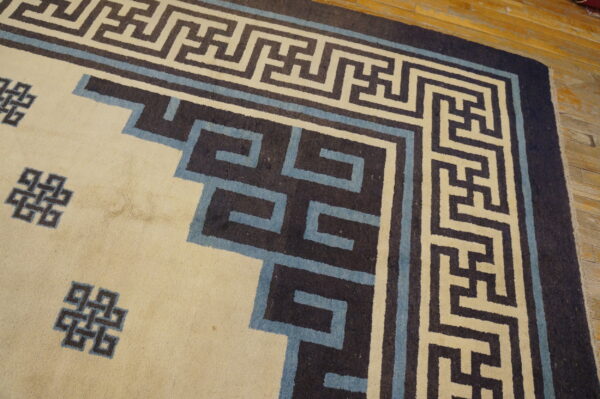 Low-pile cream rug featuring a dark brown and blue geometric border on distressed wood floor.