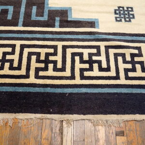 Black, cream, and blue rug border featuring a geometric meander pattern resting on exposed wood planks.