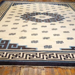 Cream rug with dark blue and brown geometric patterns and border laid over wood planks.