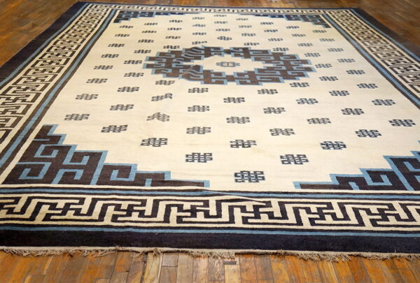 Cream rug with dark blue and brown geometric patterns and border laid over wood planks.