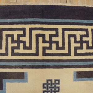 Close-up showing a cream and dark blue geometric key pattern rug border on distressed wood flooring.