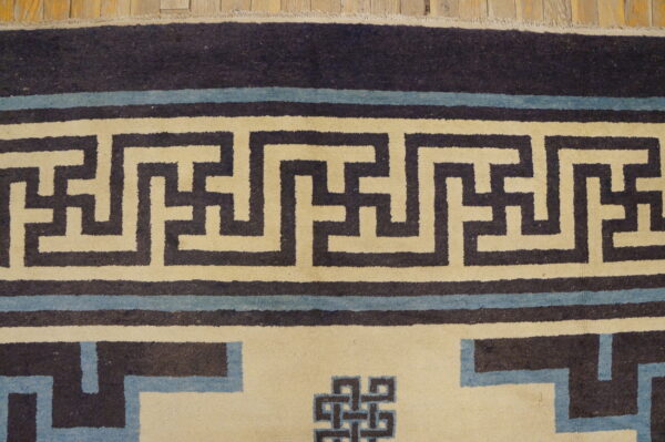 Close-up showing a cream and dark blue geometric key pattern rug border on distressed wood flooring.
