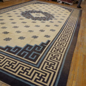 Low-pile rug with geometric patterns in cream, dark brown, and light blue on worn wood flooring.