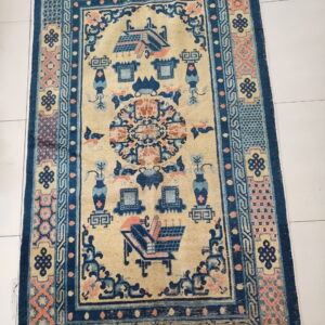 Cream rug with complex blue and peach figures and geometric borders on a light tiled floor.