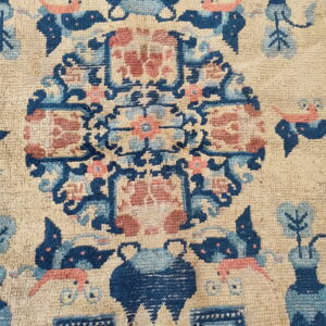 Textured rug detail showing a stylized medallion pattern in dark blue, light blue, and coral on tan.
