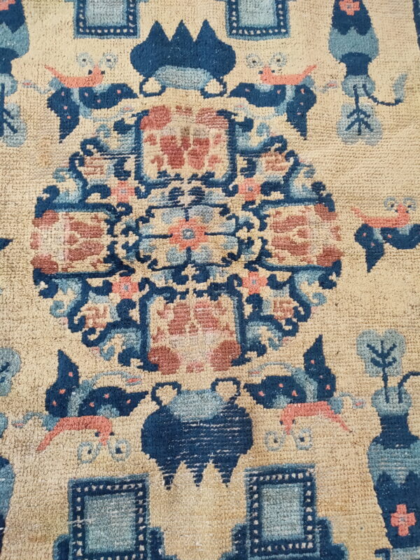 Textured rug detail showing a stylized medallion pattern in dark blue, light blue, and coral on tan.