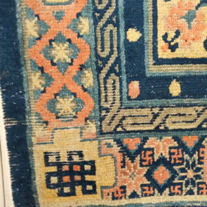 A high-pile rug detail showing navy blue, gold, and coral traditional patterns over white floor tiles.