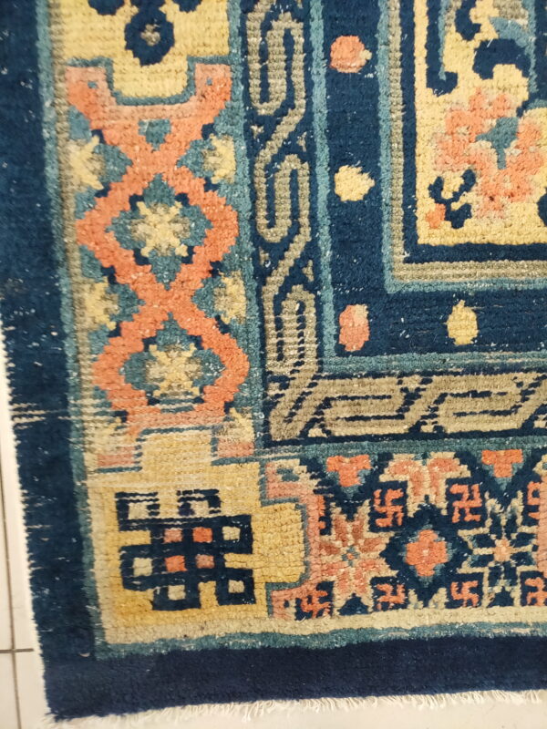 A high-pile rug detail showing navy blue, gold, and coral traditional patterns over white floor tiles.