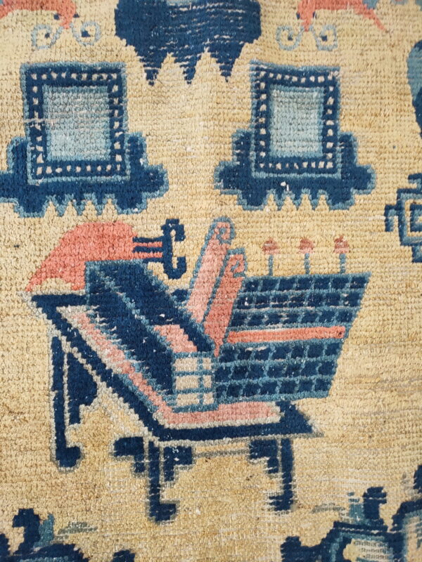 Tan rug detail featuring stylized structures and vessels in indigo, light blue, and coral pink.