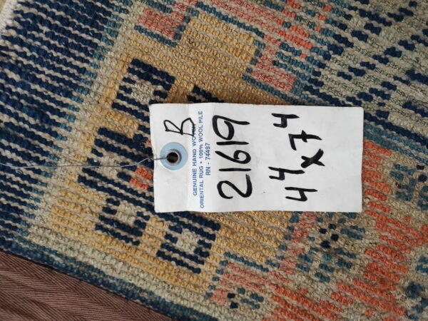 Navy, tan, and coral low-pile rug with a geometric pattern, partially obscured by a large product tag.