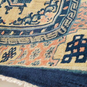Medium pile rug detail featuring beige, navy, peach, and teal geometric patterns and fringe.