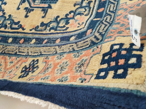 Medium pile rug detail featuring beige, navy, peach, and teal geometric patterns and fringe.