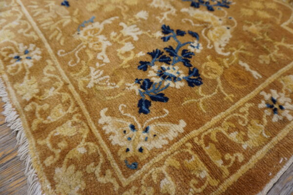 Close-up of a gold, medium-pile floral rug with cream, yellow, and vibrant blue accents on wood flooring.