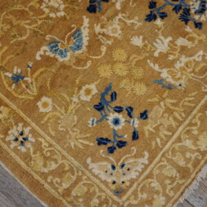 Golden tan rug corner featuring blue and cream floral patterns and a butterfly on gray wood planks.