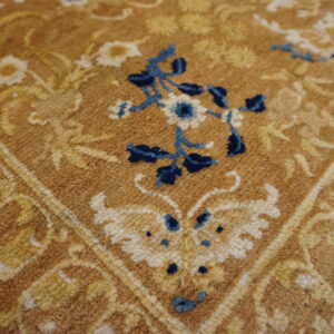 Close-up texture of a shaggy rug featuring blue and gold floral patterns on a tan background.