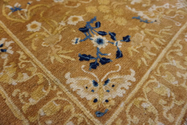 Close-up texture of a shaggy rug featuring blue and gold floral patterns on a tan background.