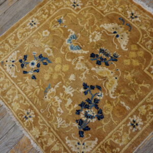 Golden-brown low-pile area rug with elaborate blue and cream floral designs on rustic wooden planks.