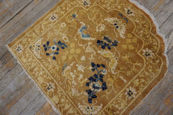 Golden-brown low-pile area rug with elaborate blue and cream floral designs on rustic wooden planks.