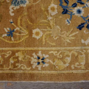 Close-up of a tan rug with floral patterns in yellow, ivory, and dark blue on wood plank flooring.