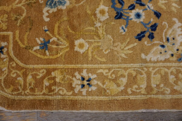 Close-up of a tan rug with floral patterns in yellow, ivory, and dark blue on wood plank flooring.