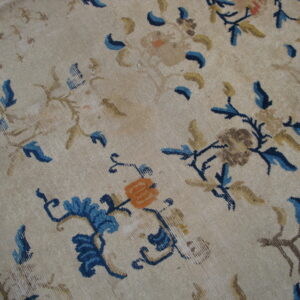 Light beige rug surface patterned with scattered blue, gold, and orange stylized floral motifs.