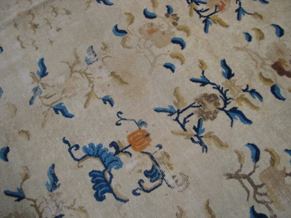 Light beige rug surface patterned with scattered blue, gold, and orange stylized floral motifs.