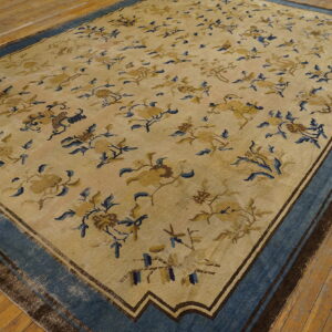 Large beige rug with an all-over blue and gold floral pattern and a wide blue border on wood floors.