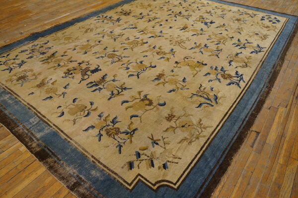 Large beige rug with an all-over blue and gold floral pattern and a wide blue border on wood floors.