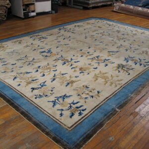 A large cream rug with scattered blue and tan florals and a wide blue border lies on wood floors.