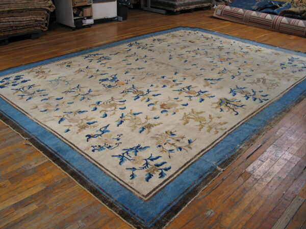 A large cream rug with scattered blue and tan florals and a wide blue border lies on wood floors.