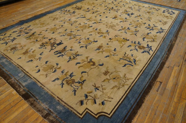 Large beige rug with scattered blue and gold floral patterns and a wide blue border on wood floors.