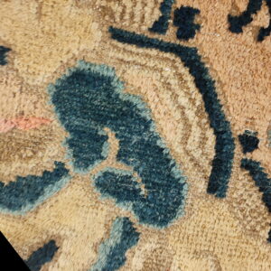 Macro view of a high pile rug with stylized dark blue motifs on a mottled beige and tan ground.