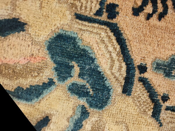 Macro view of a high pile rug with stylized dark blue motifs on a mottled beige and tan ground.