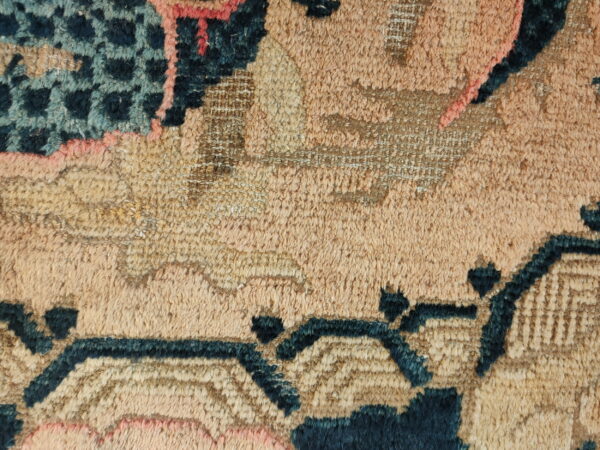 Detailed texture of a rug featuring high pile in tan and peach with contrasting dark teal patterns.