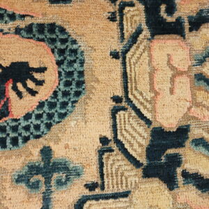 Detailed view of a high-pile rug with tan field, dark stylized patterns, coral accents, and checkerboard texture.