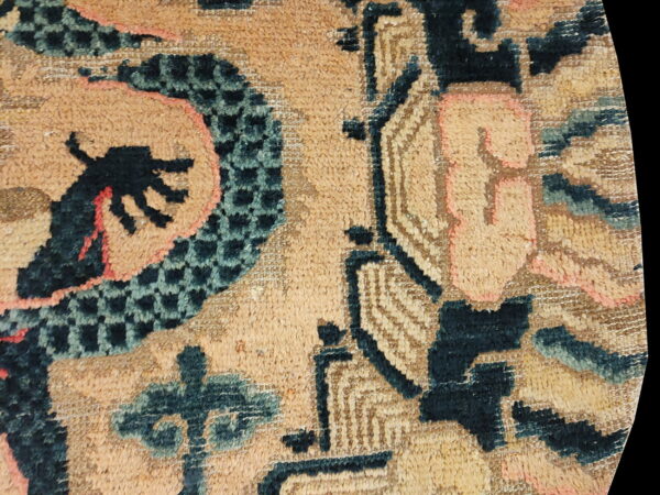 Detailed view of a high-pile rug with tan field, dark stylized patterns, coral accents, and checkerboard texture.